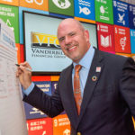 Steve Distante in front of a poster of the Sustainable Development Goals set by the United Nations
