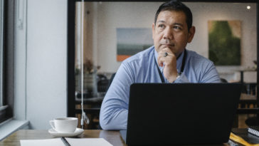Thoughtful ethnic businessman using laptop while working in office
