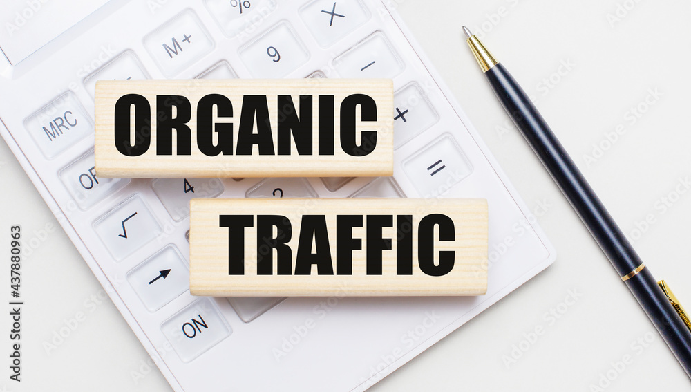 Wooden blocks with the text ORGANIC TRAFFIC lie on a light background on a white calculator. Nearby is a black handle. Business concept
