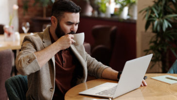 Man drinking coffee while looking at his laptop