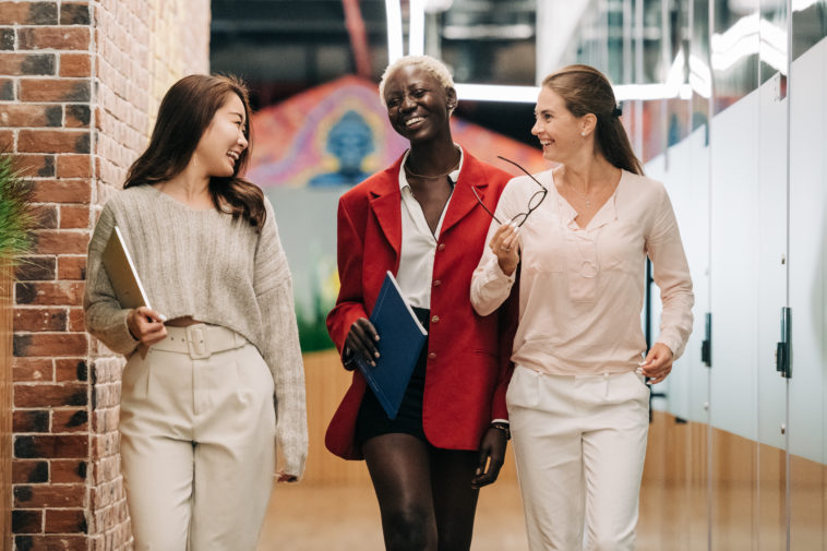 Diverse successful businesswomen smiling and walking together in modern workplace