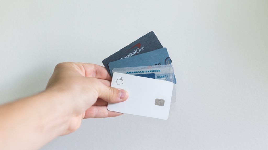 A person holding credit cards against a white background wall.